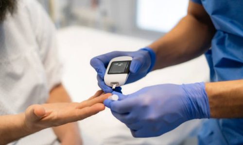 Doctor is using glucometer for measuring blood glucose level of patient in hospital room